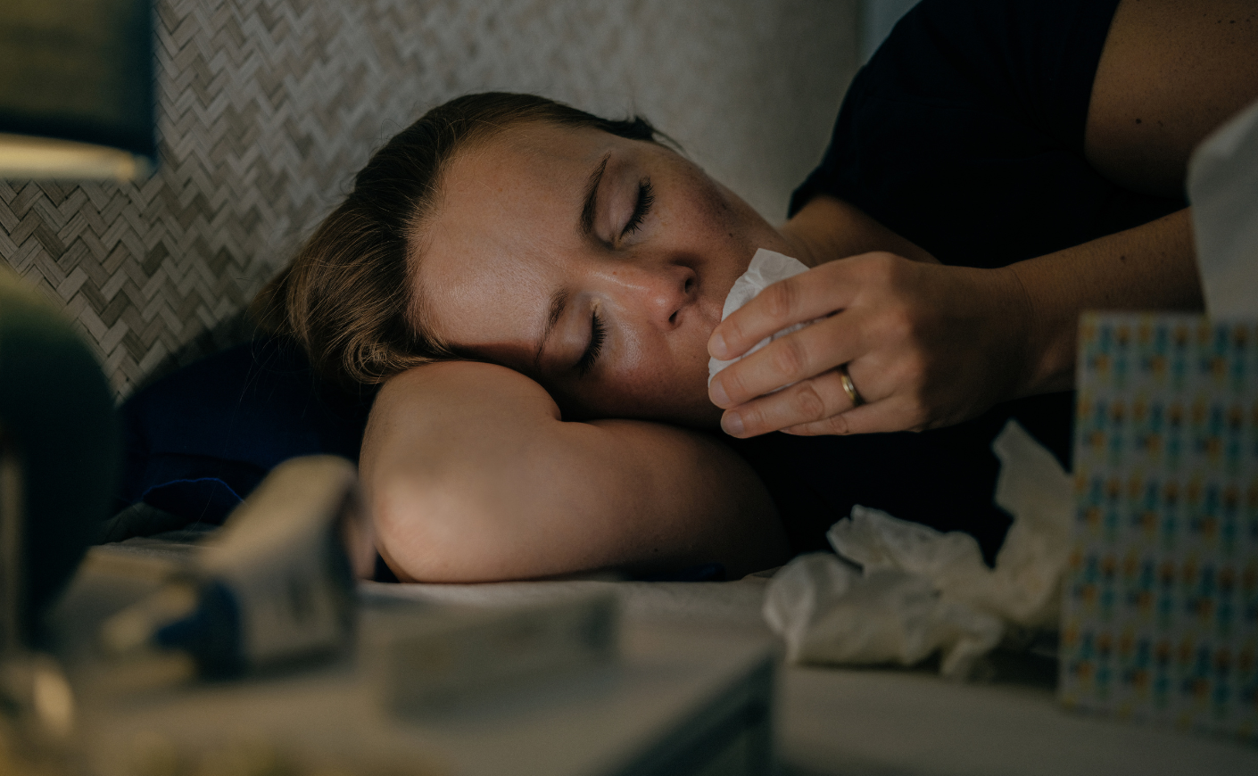 A sick woman lying in bed with tissues