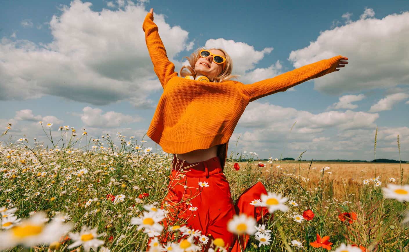 a woman joyfully raises her arms in a field of flowers