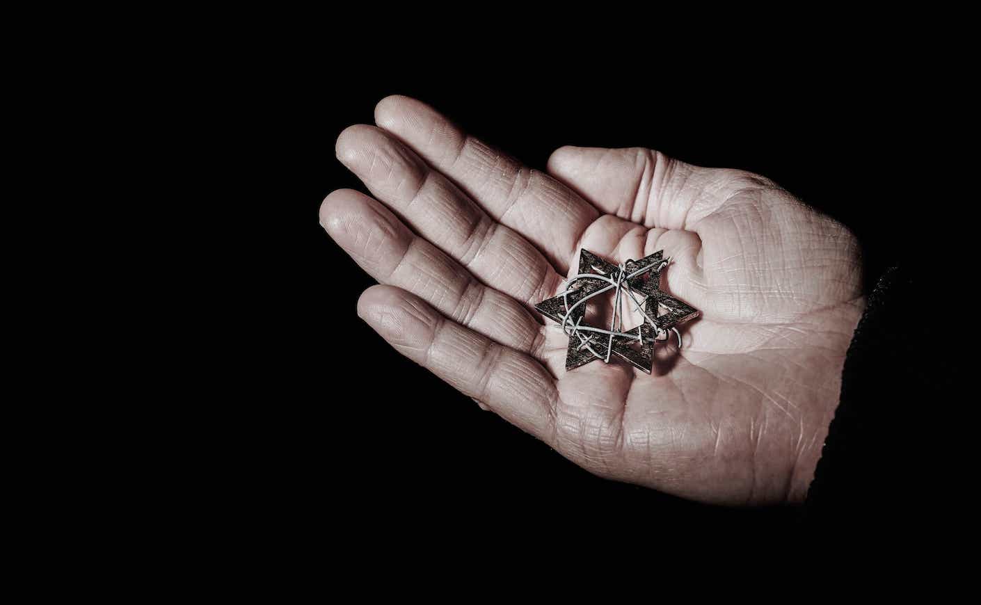 a hand holding a jewish star wrapped in barbed wire