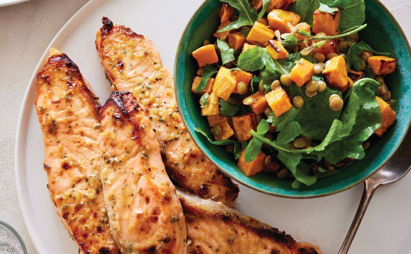 Two air fried salmon fillets next to a small bowl of roasted sweet potato and lentil salad.