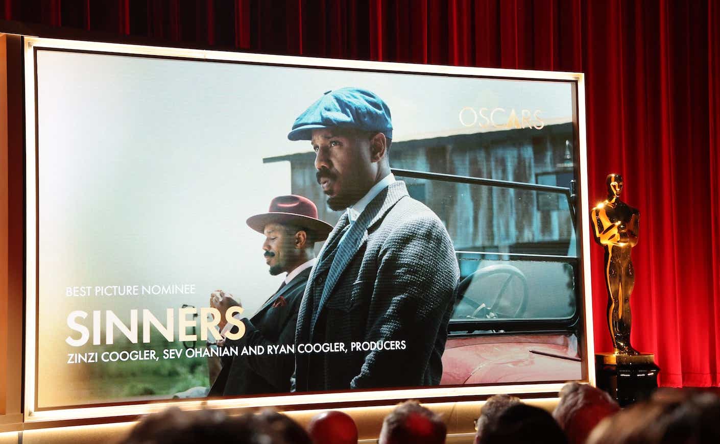 a screen showing an still from the film sinners with michael b jordan, with a oscar trophy statue next to it