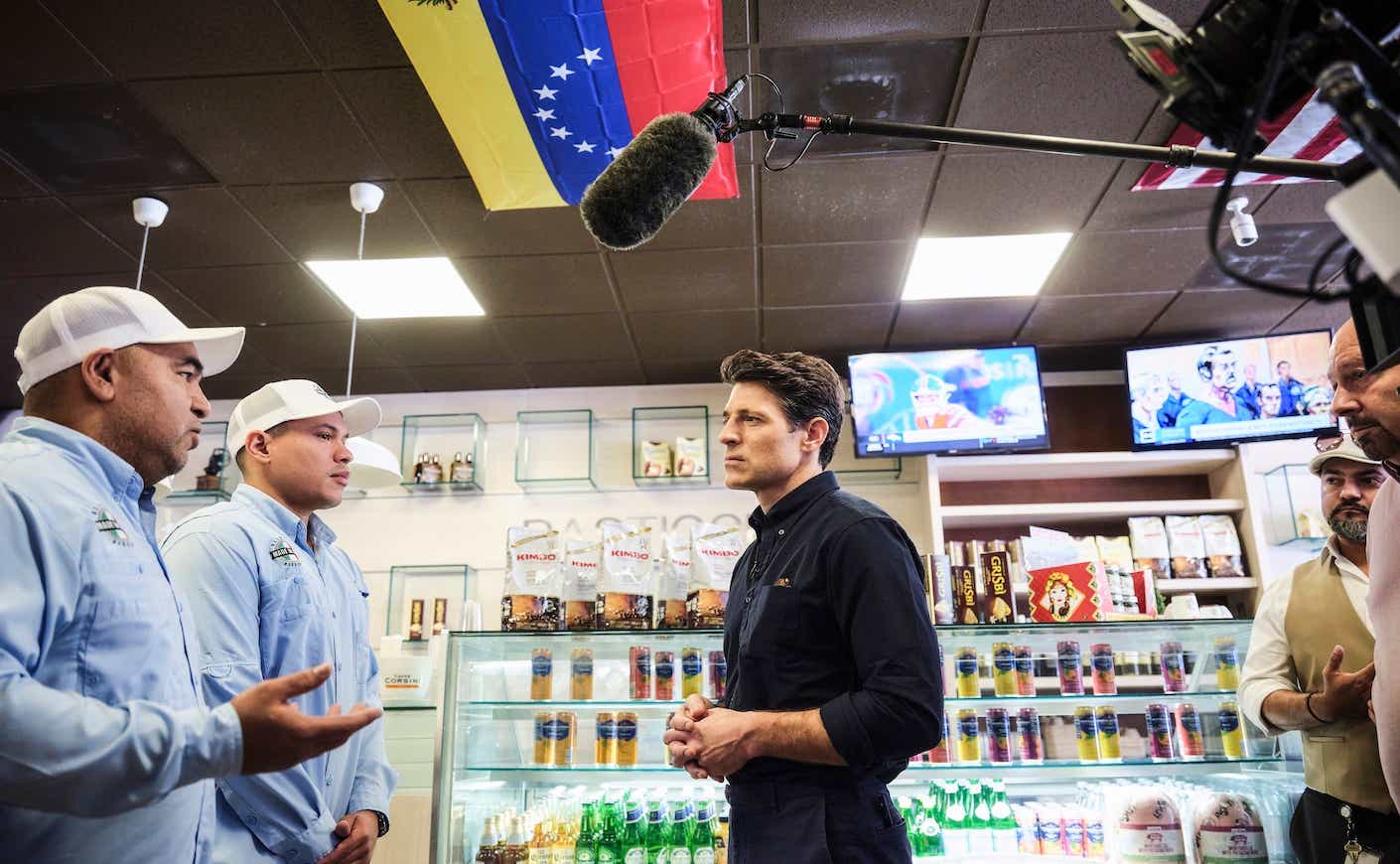 Tony Dokoupil reporting a segment of CBS evening news from Doral, FL, intervieweing two male shop owners