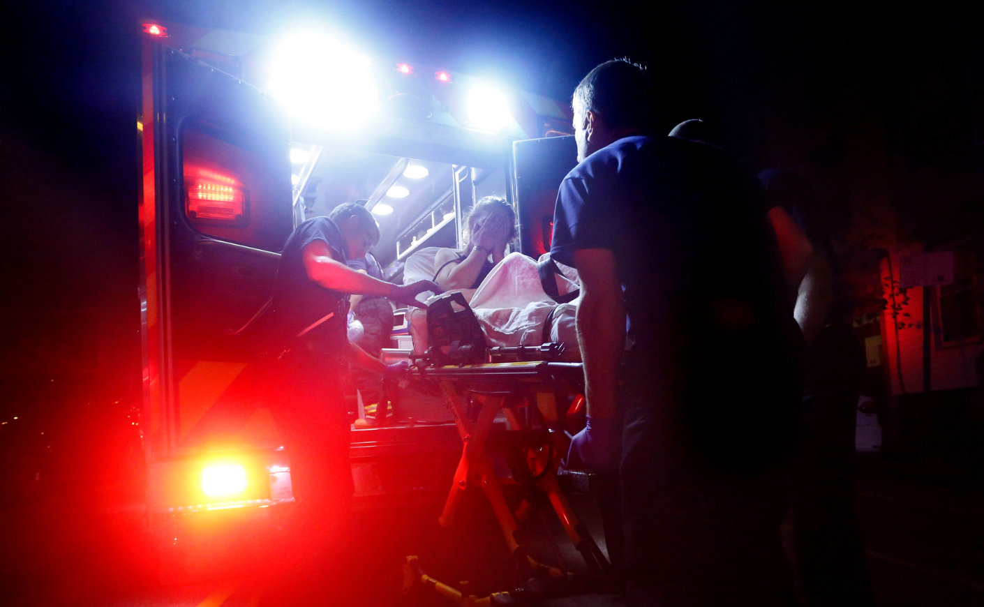 EMTS loading a distressed woman onto an ambulance at night.
