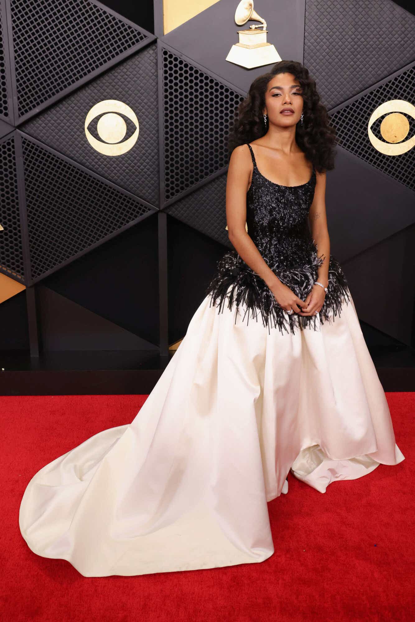 Olivia Dean wears a two-toned gown. The top half is a black lace and the bottom is a full white ballgown skirt. The bodice is feathered where it meets the skirt.