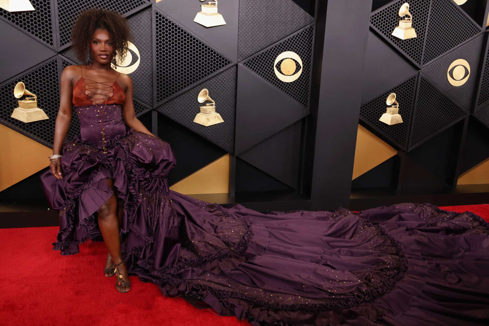 Doechii wears a dress with an open corseted red top and a very dramatic ruffled purple skirt with a long train.