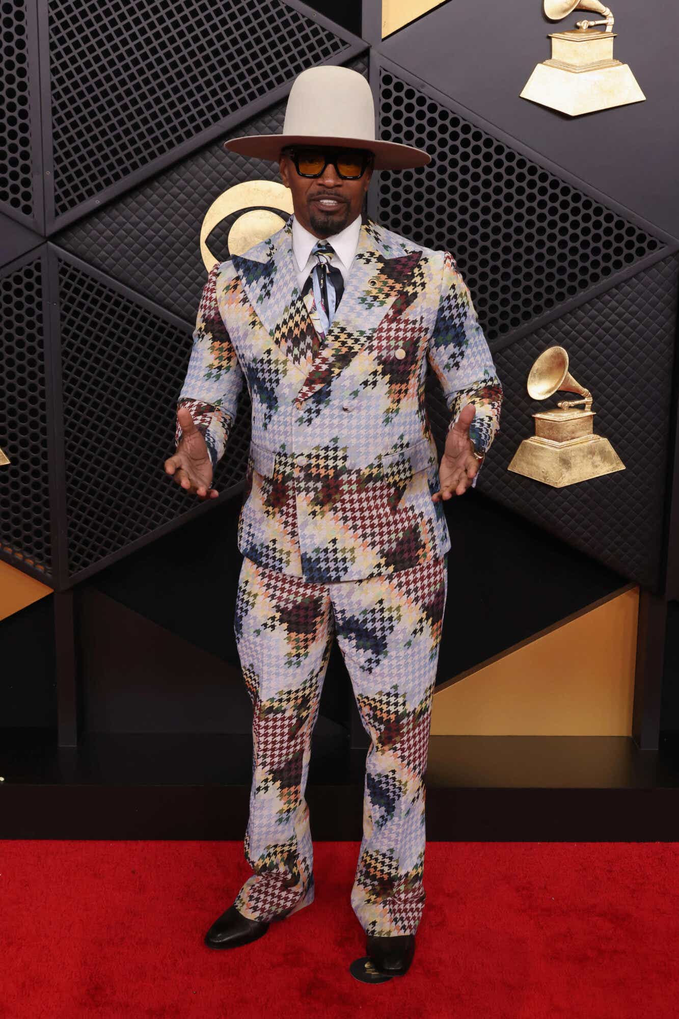 Jamie Foxx wears a brown, cream, blue and black houndstooth print suit and a matching wide-brimmed cream-colored hat.