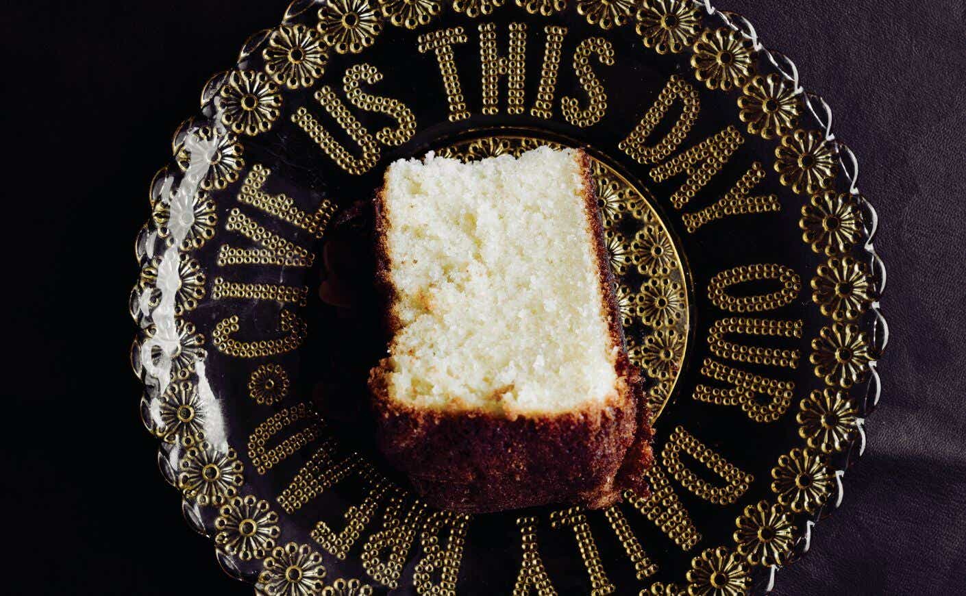 A slice of olive oil cake on a plate that says "give us this day our daily bread."