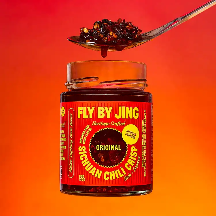 A spoon full of chili crisp and a jar of Fly By Jing's.