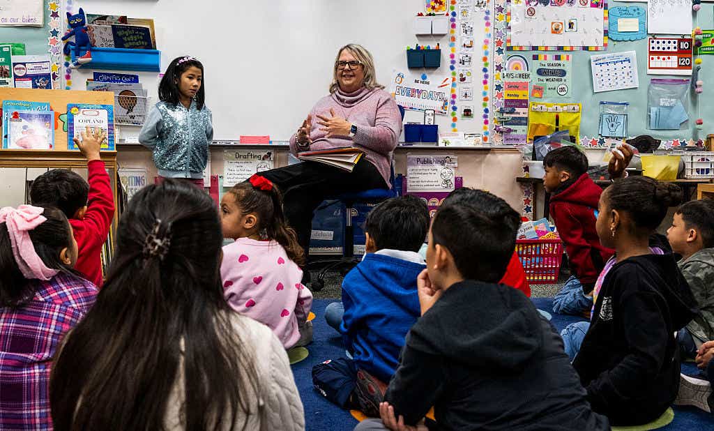 A teacher at the front of a class filled with students.