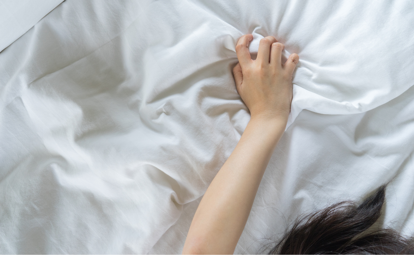 Close-up of a woman's hand clutching the sheets in bed