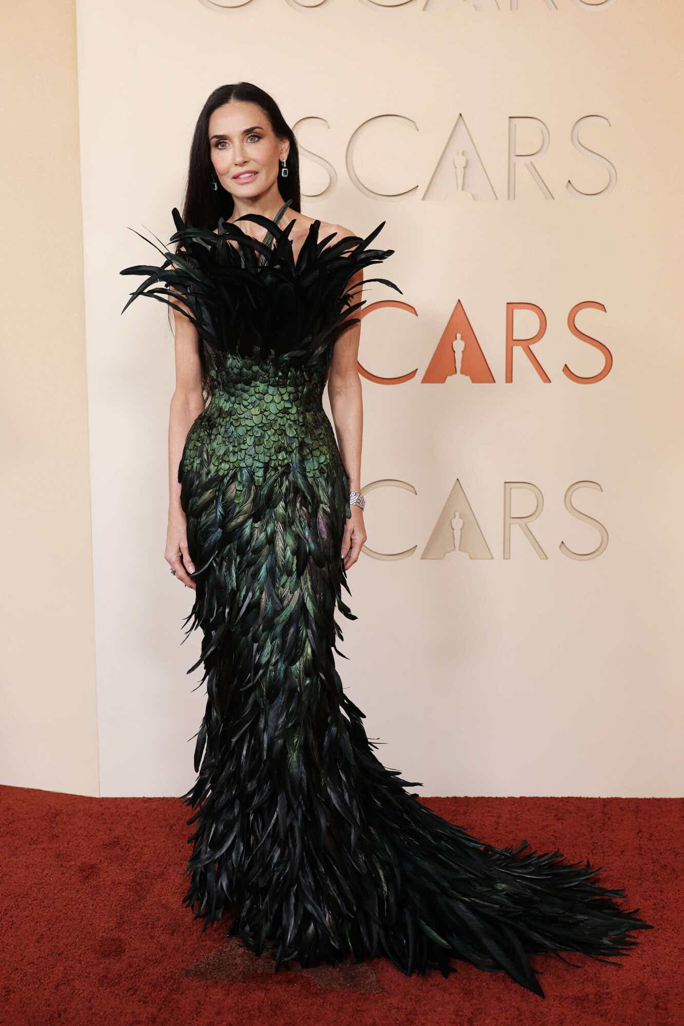 Demi Moore wears a fully feathered gown that fades from black to green back to black.