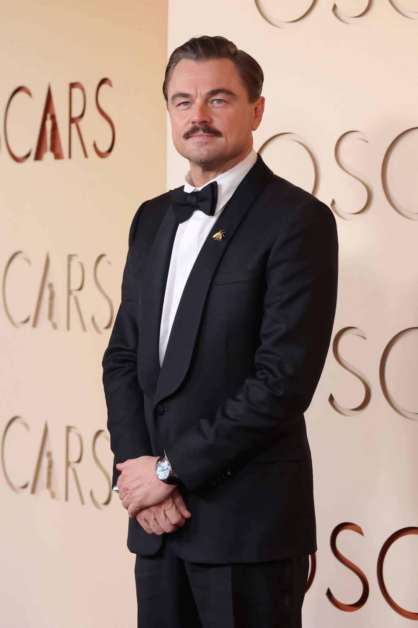 Leo DiCaprio wears a black tux with a small gold bee pin affixed to the lapel.