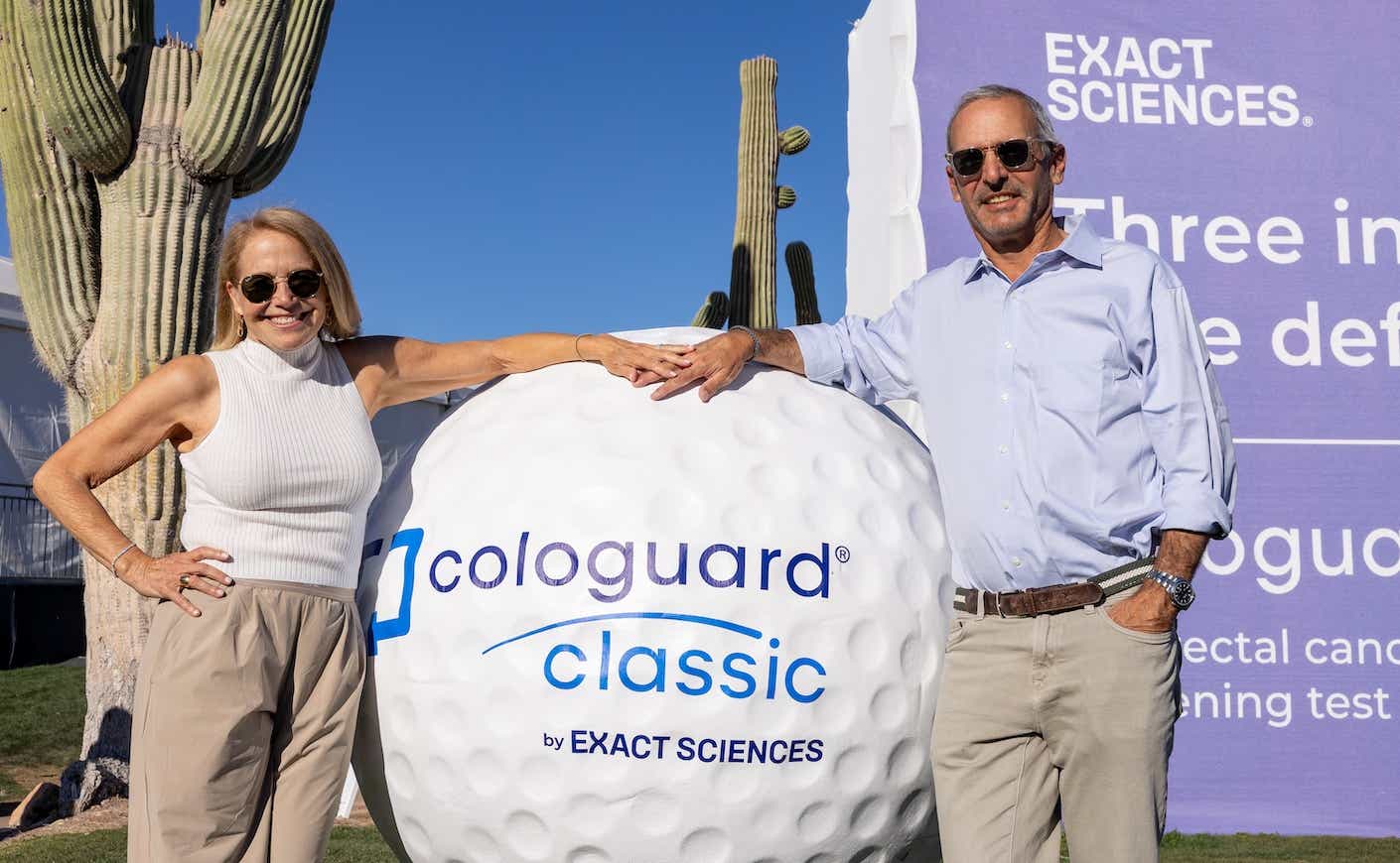 katie couric and john molner posing with a giant golf ball that says "cologuard classic by exact sciences"