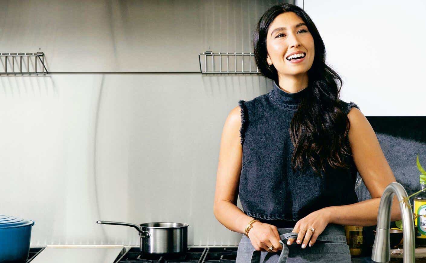 Maxine Sharf in a kitchen tying an apron around her waist.