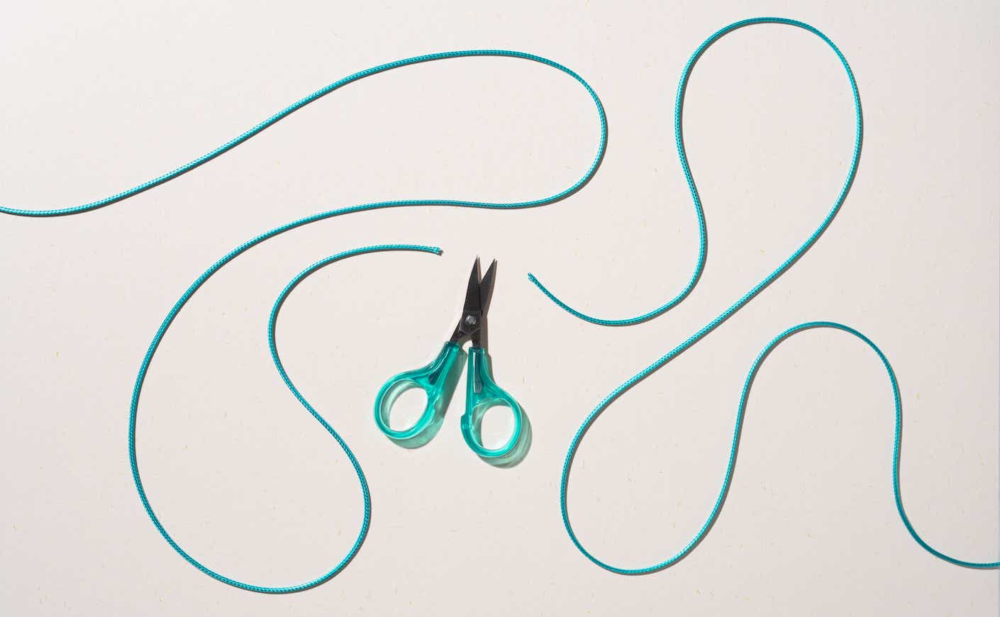 Green Colored Scissors Cut Curved Rope on Beige Background Directly Above View.