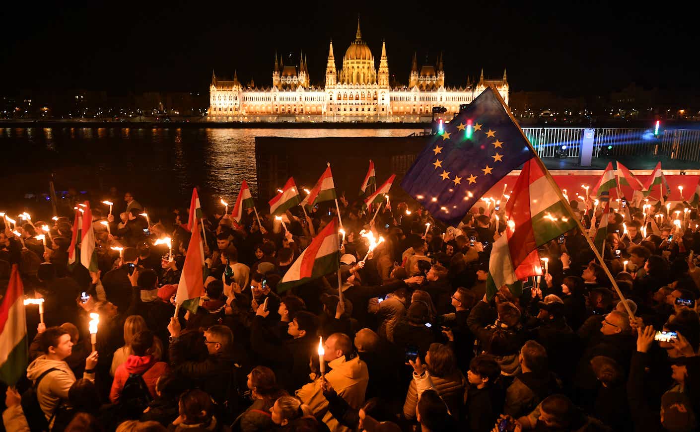 Supporters of the pro-European conservative TISZA party celebrate during the election night on the banks on the river Danube with the Parliament building in the background, in Budapest after the general election in Hungary, on April 12, 2026. Polls closed in Hungary's parliamentary election, with turnout reaching a record high in the crunch vote that sees nationalist Prime Minister Viktor Orban's 16-year stint in power face an unprecedented challenge from conservative political newcomer Peter Magyar. (Photo by Ferenc ISZA / AFP)