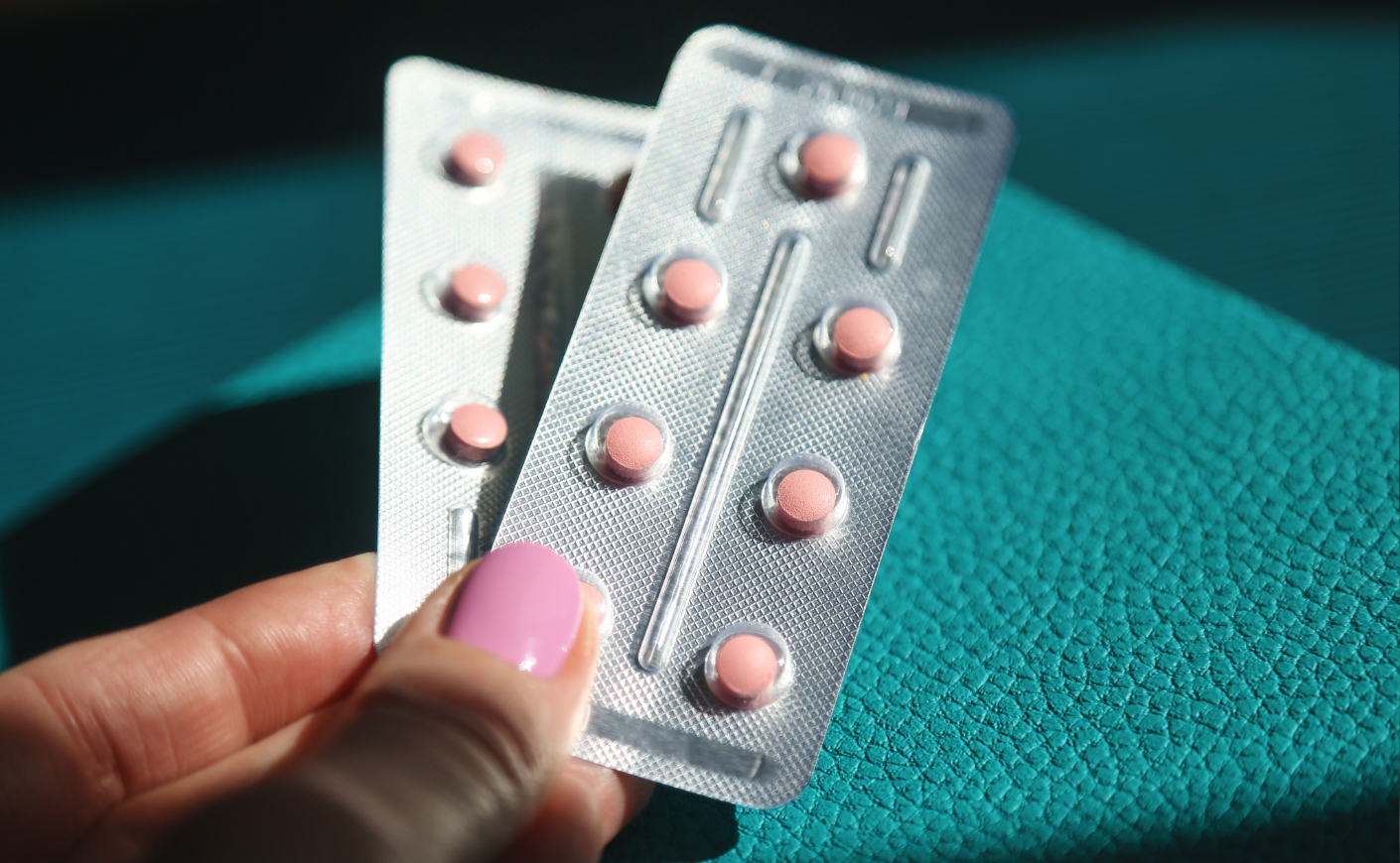Close-up of fingers holding packets of pink estrogen pills