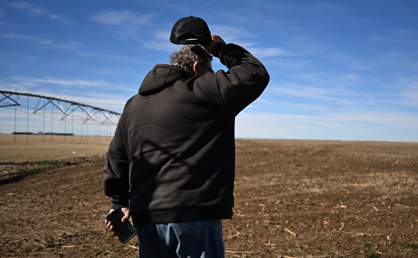 A farmer lifting his cap and looking out over an empty field.