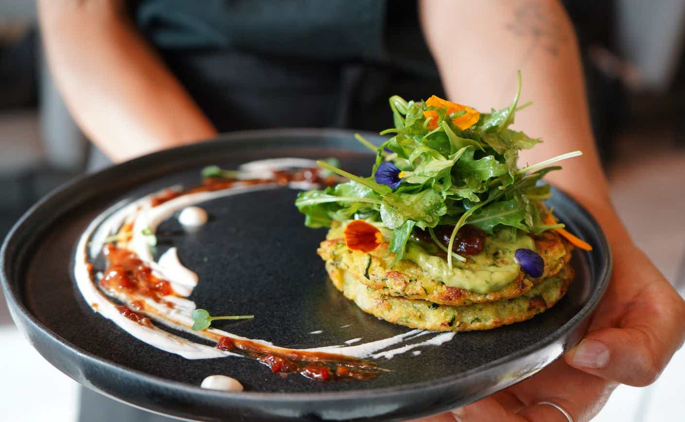 Two hands carrying a plate with a socca on it.