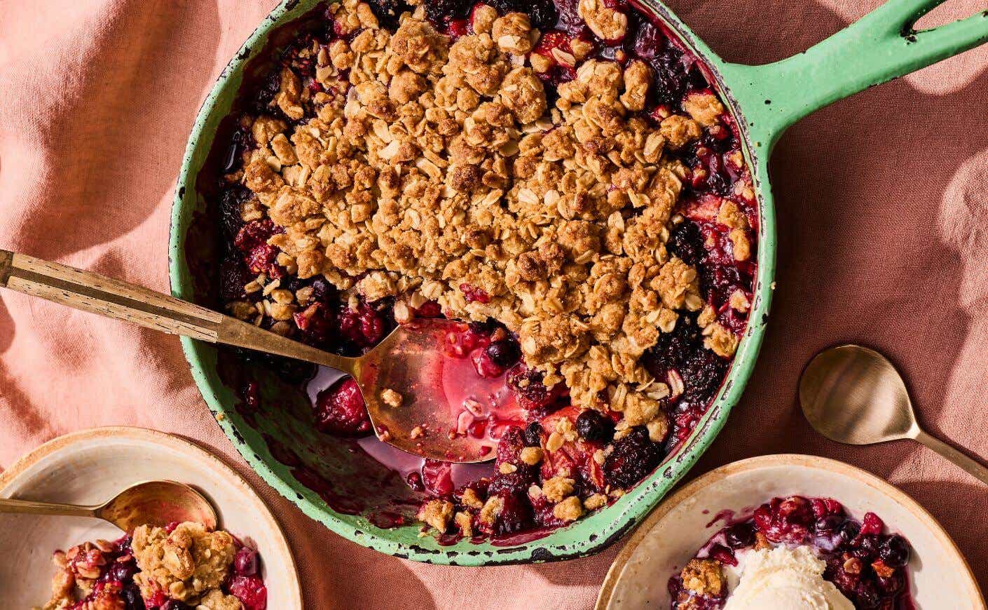 A serving spoon digging into a berry crumble in a skillet.