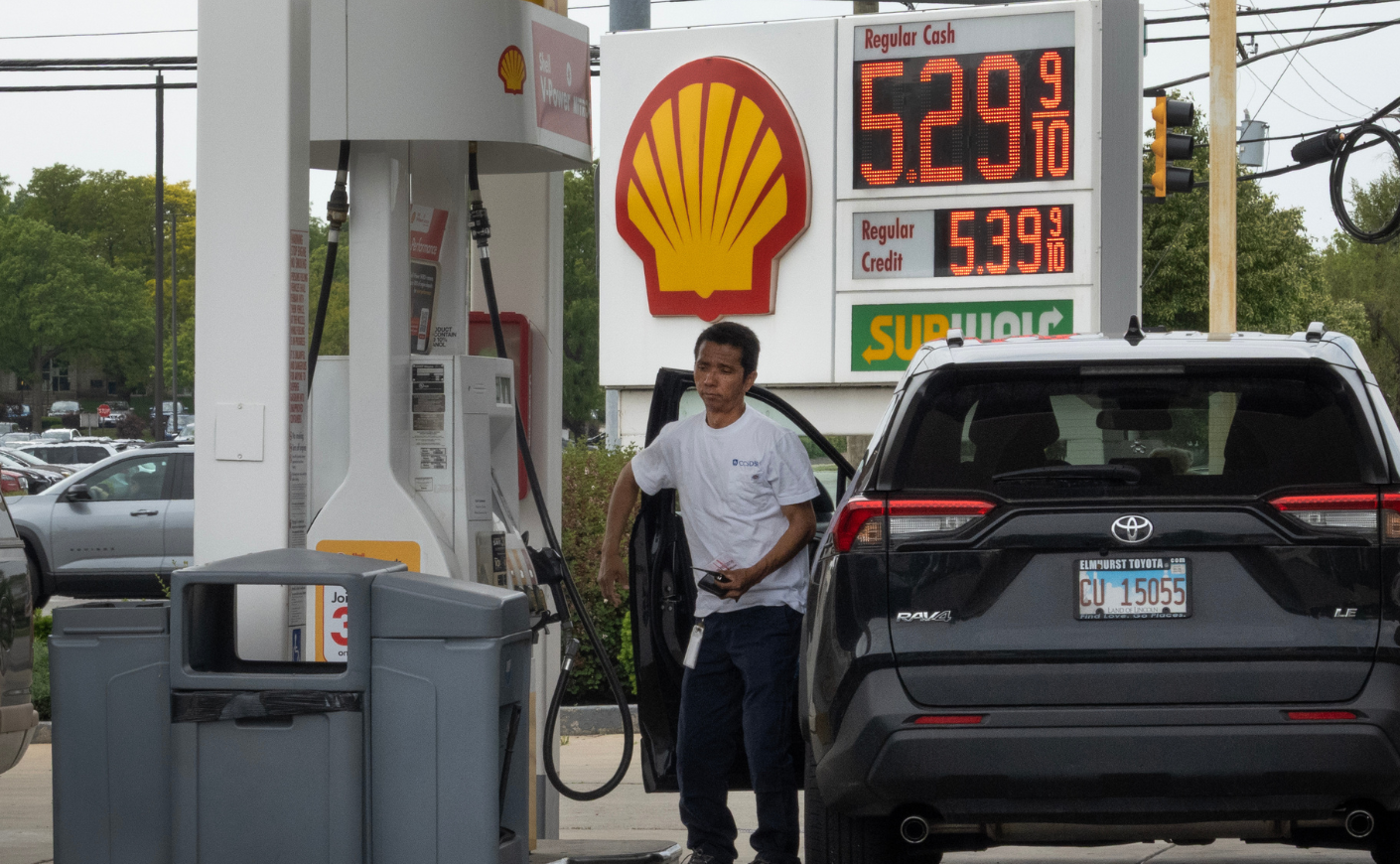 A man putting gas in a black Toyota Rav 4. behind him, gas prices read 5.29 per gallon.
