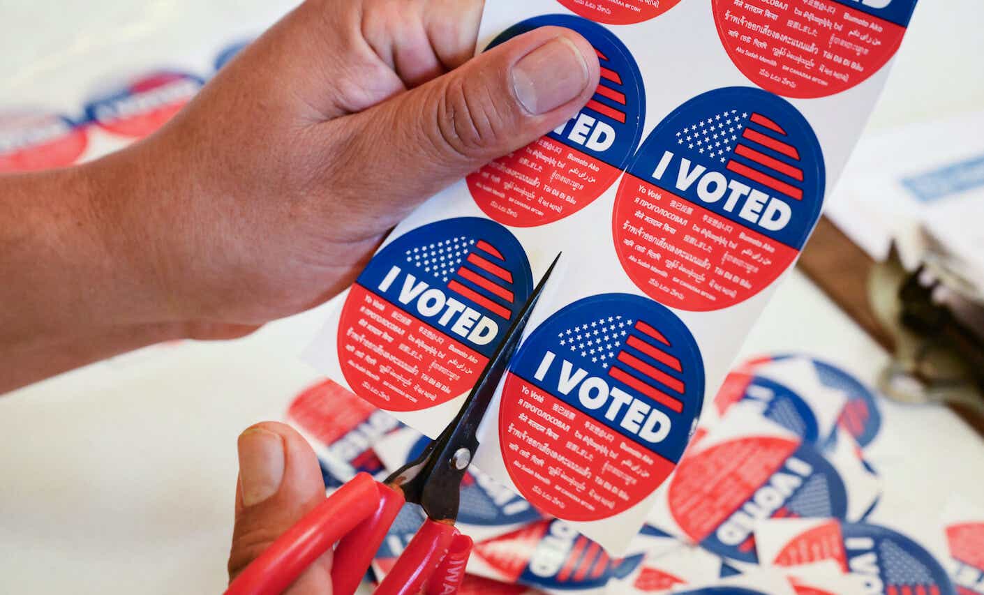 A hand using scissors to cut "I voted" stickers.