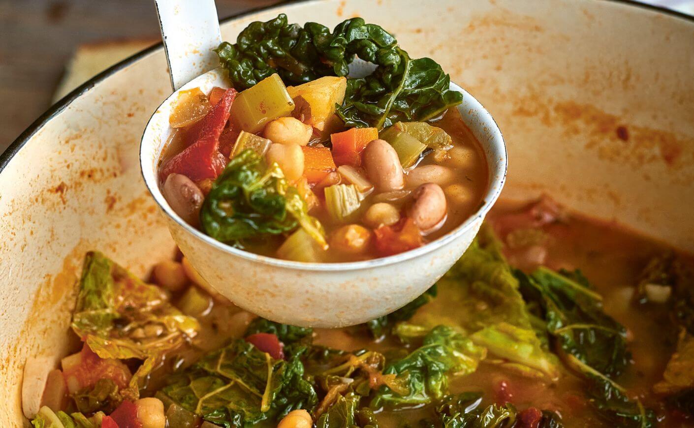 A ladle scooping minestrone from a pot.