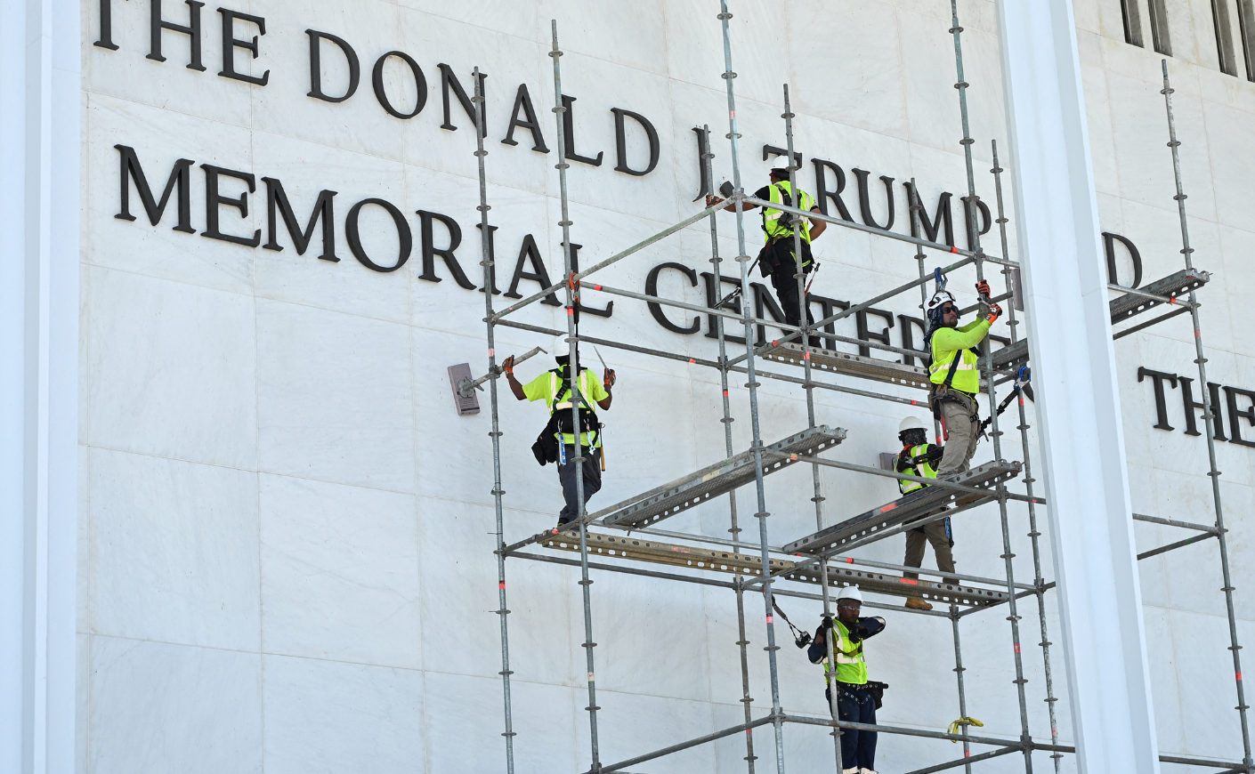 Four workers in neon yellow vests standing on scaffolding, removing Trump's name from the Kennedy Center.