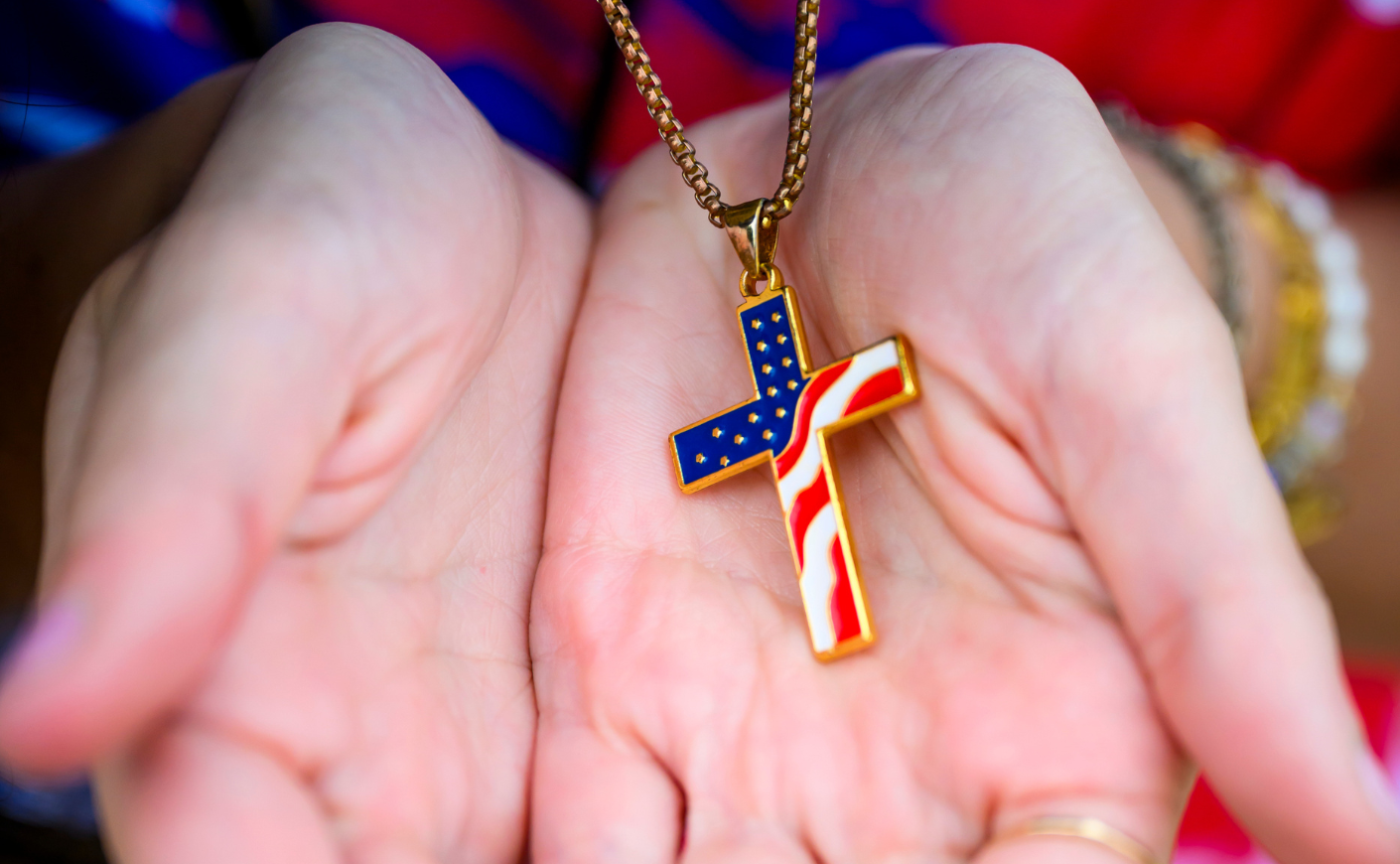 hands holding a cross charm filled in with the american flag