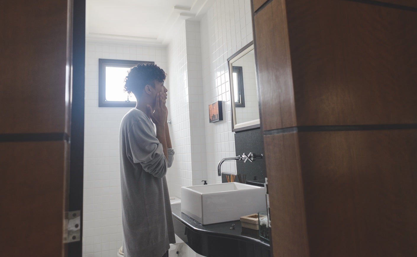 a teen boy looks at his face in the mirror