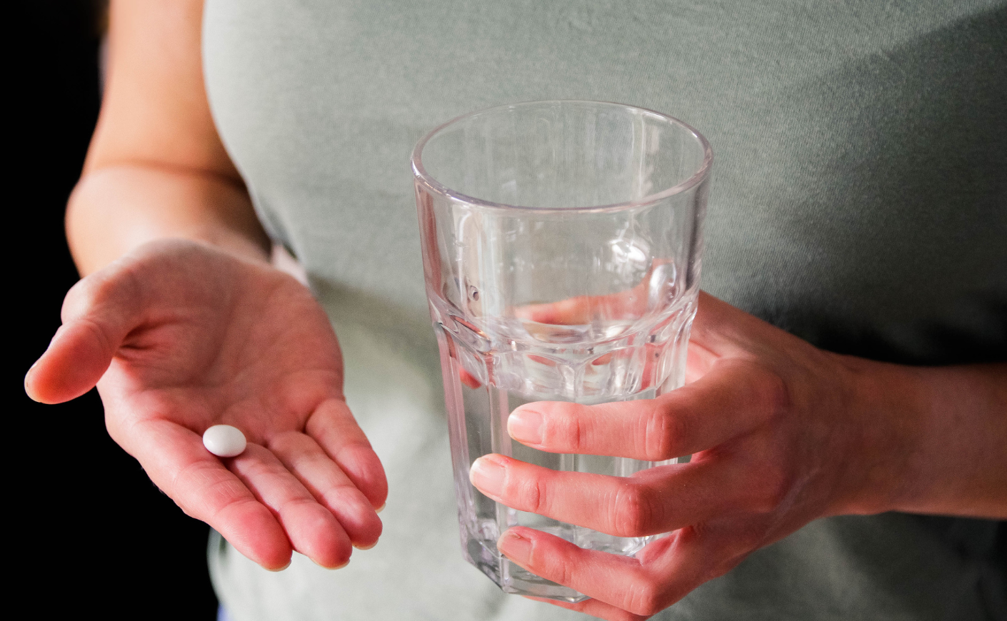 person holding pill and glass of water