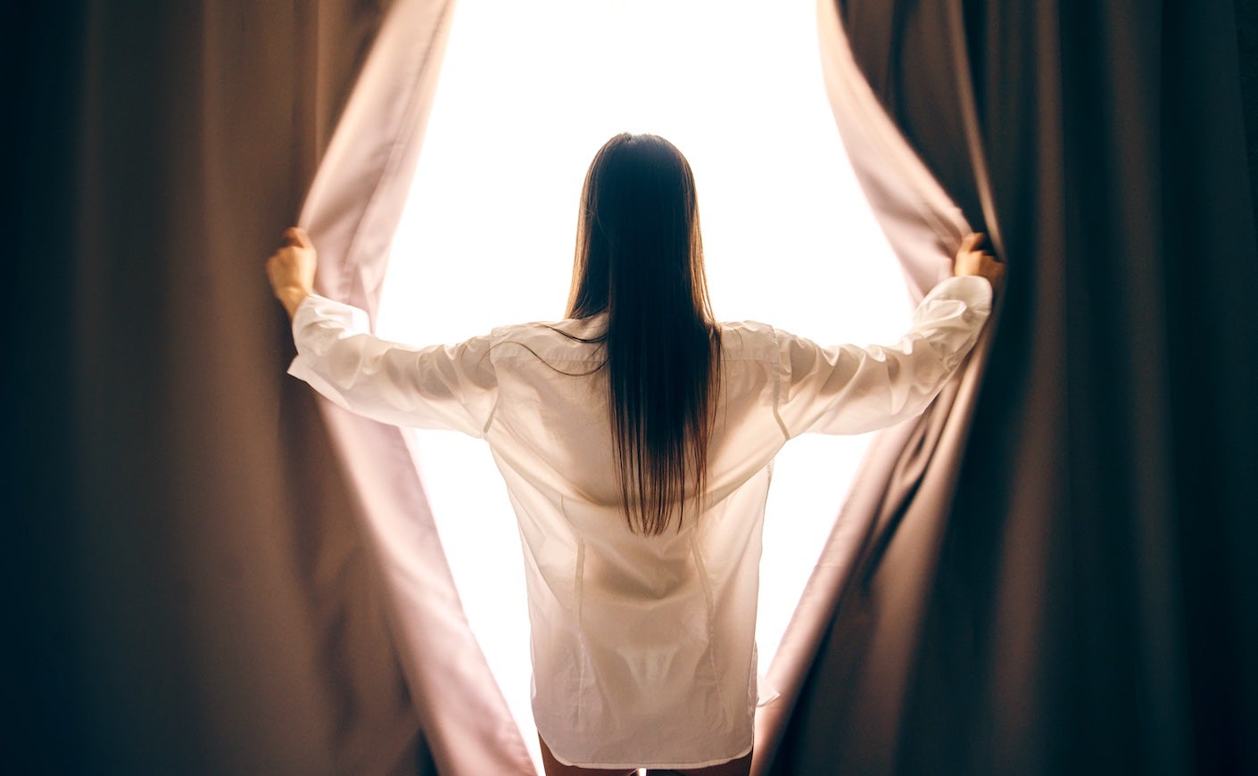 woman holding curtains open to look out window
