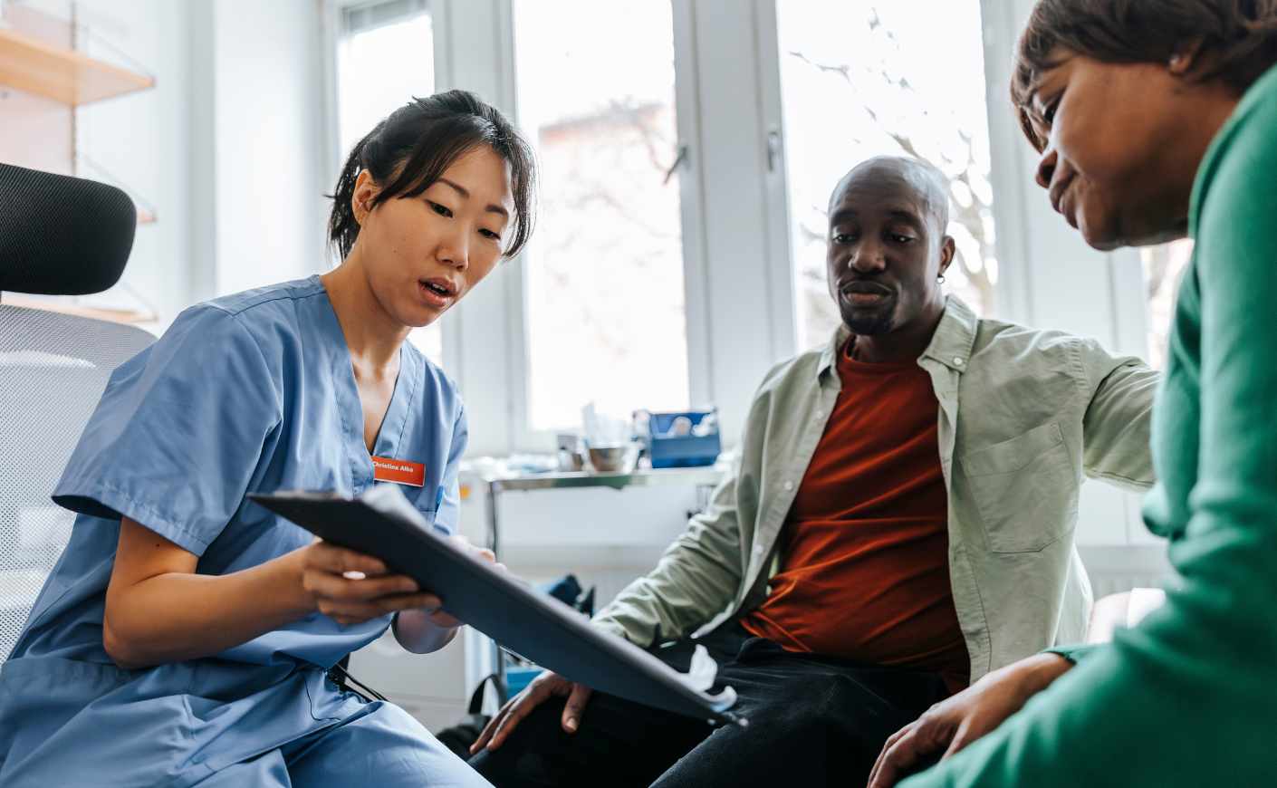An Asian woman in scrubs showing a Black man and women a scan.