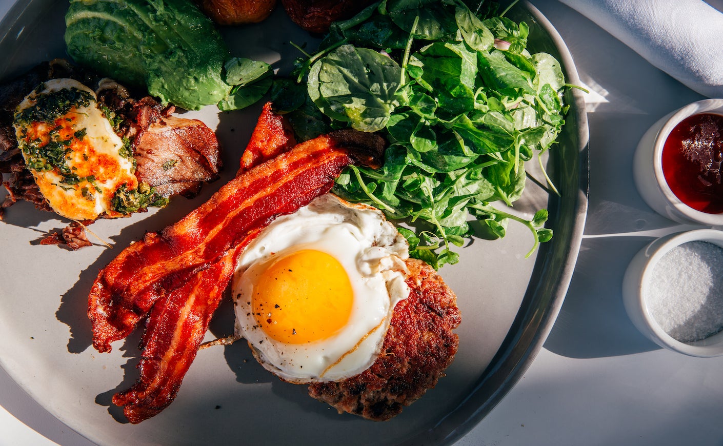 Keto breakfast with fried sunny side up egg, beef, bacon, spinach, avocado, and halloumi cheese served at a restaurant