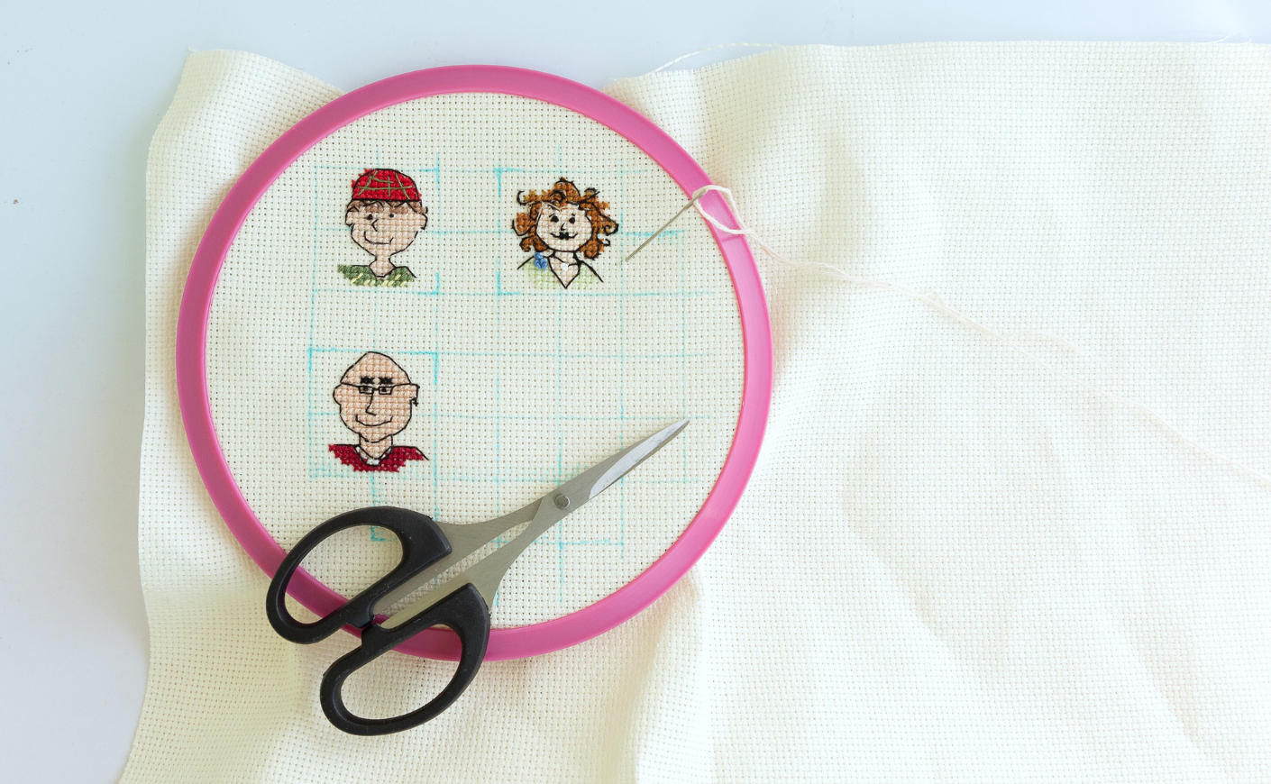 Cross stitch funny mini portraits of friends, top view of the canvas in the hoop and scissors
