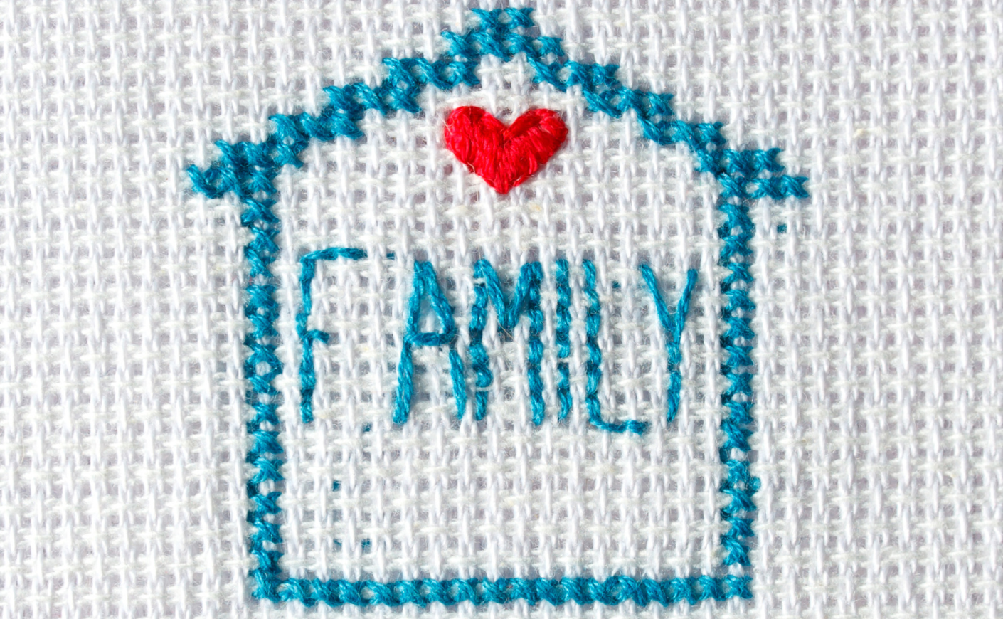 Cross stitch of a house with the word FAMILY written inside and a heart over it