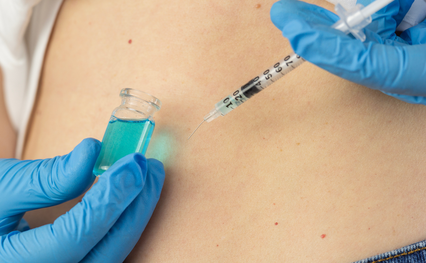 Close-up of person wearing blue latex gloves injecting a blue-green substance into their abdomen