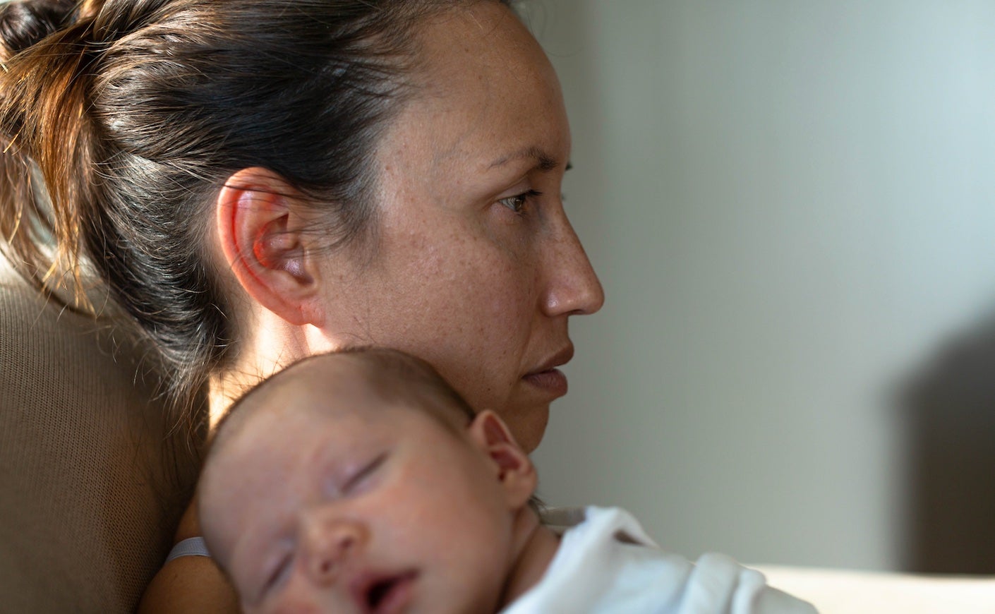 a woman stares off as her baby sleeps on her shoulder
