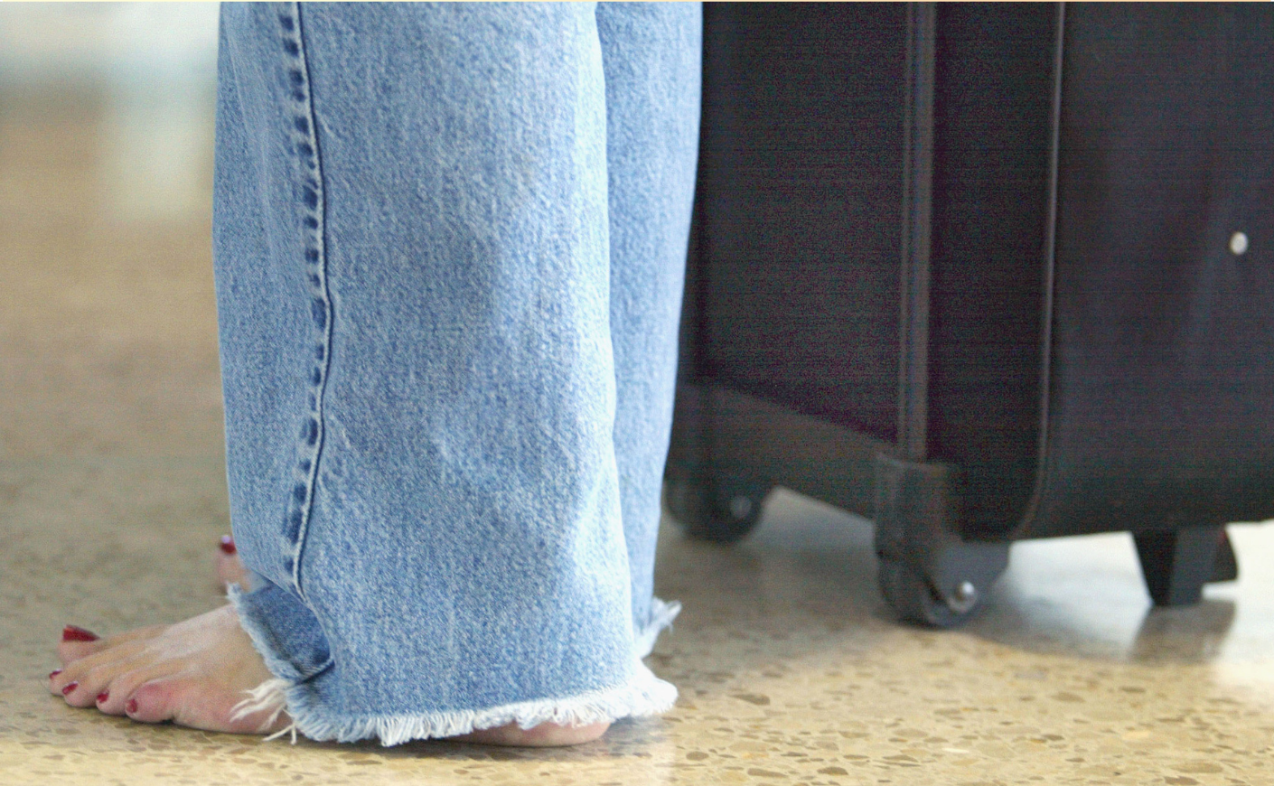 Close-up of woman standing barefoot in the airport with her luggage