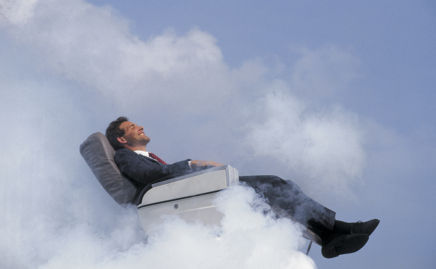 A businessman reclining on an airplane seat in the clouds