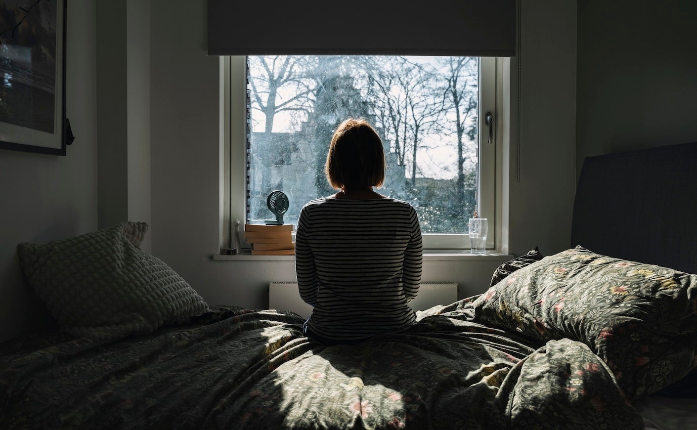 Rear view of a mature woman looking out of her bedroom window on a bright winter's day