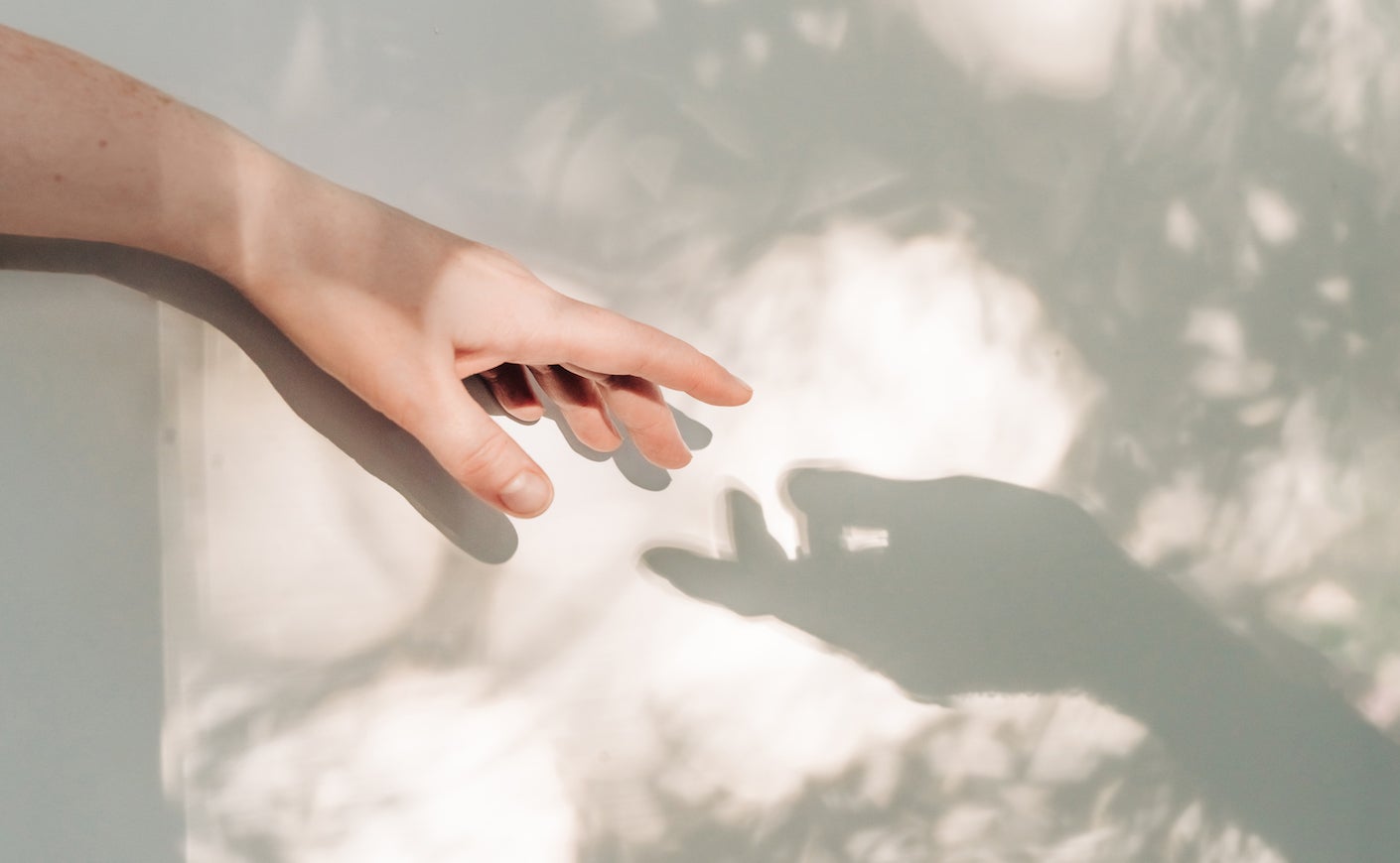A human hand reaching toward its own shadow cast on a textured surface.