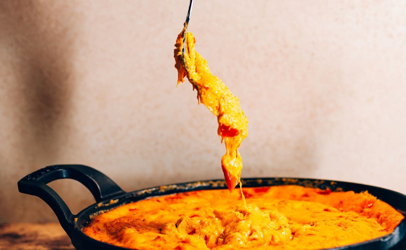A fork dipping into a pot of cheese dip.