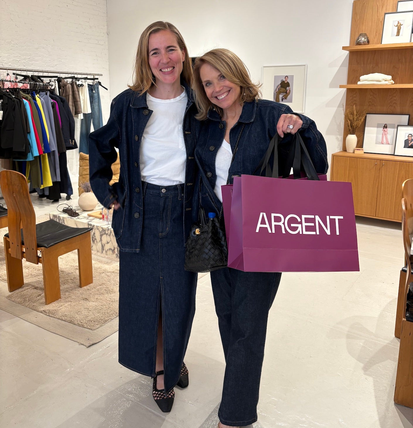 two women posing in a store, katie couric holding up a shopping bag that says argent