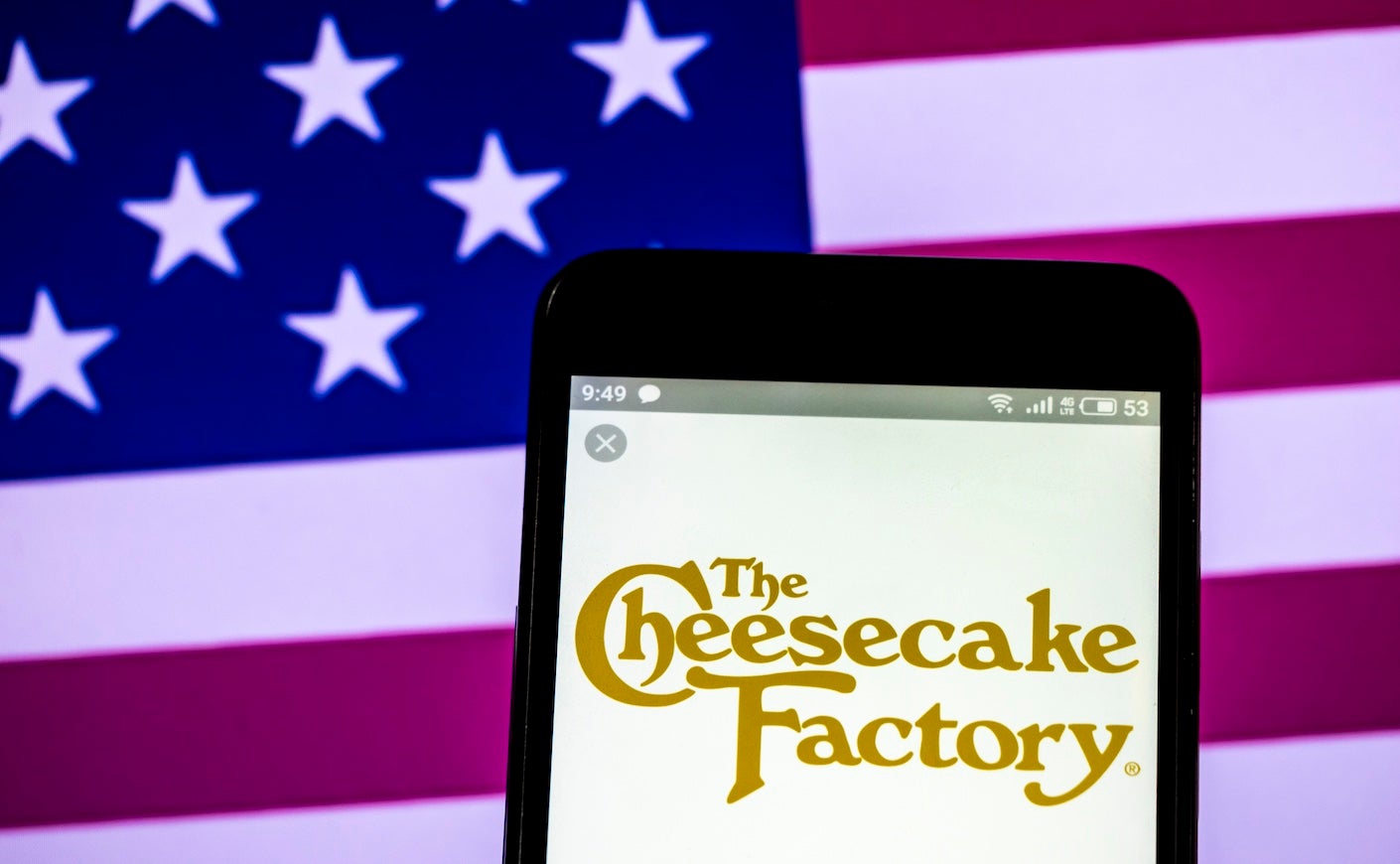cheesecake factory logo on a phone in front of the america flag