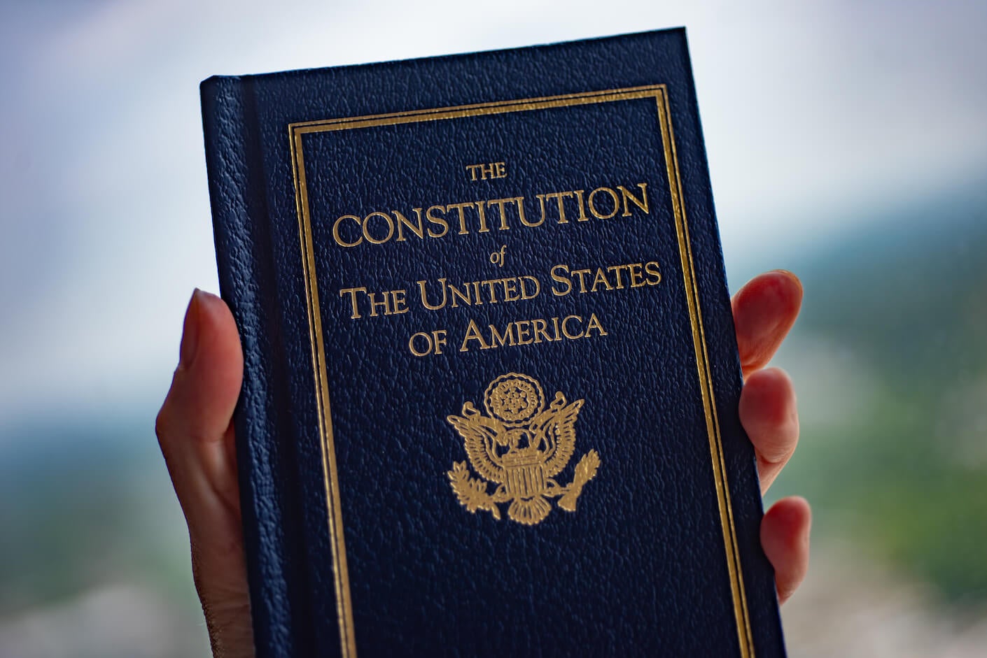 The Constitution of The United States of America book in hand on a blurred background.