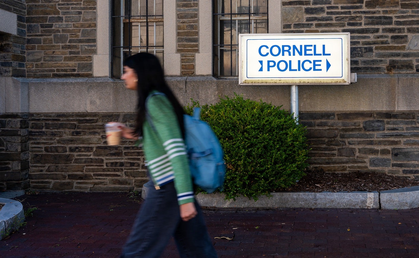 young female student walking by a stone building with the sign "cornell police"